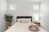 Serene bedroom with plush bedding, natural lighting, and stylish decor including a potted plant and cozy bedside lamp.