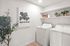 Bright and modern laundry room featuring a washer, dryer, stylish wall art, and shelving with potted plants and storage, ideal for a functional and chic home space.