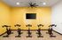Modern indoor cycling studio with sleek stationary bikes, vibrant yellow accent wall, and mounted TV for entertainment.