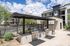 Modern outdoor BBQ area with sleek grills and shaded seating, set against a backdrop of stylish apartment buildings and lush landscaping.