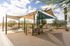 Charming outdoor playground with shaded canopies, surrounded by natural landscaping and a picnic table for relaxation.
