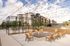 Modern apartment complex with elegant outdoor seating area featuring stylish Adirondack chairs, ambient string lights, and lush greenery for a serene living experience.