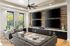 Modern living room with sleek gray sofas, rustic wood-paneled wall featuring multiple flat-screen TVs, large windows with natural light and cacti, creating a stylish and cozy entertainment space.