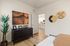 Inviting bedroom with elegant decor, featuring a stylish dresser, vibrant plant, and a glimpse into a modern kitchen beyond.