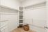 Spacious walk-in closet with white shelving and a woven basket on a wood floor, perfect for organized storage.