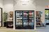 Modern convenience store interior featuring a well-stocked fridge with beverages, snacks on sleek shelves, and a stylish checkout counter with a potted plant.