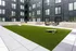 Modern apartment courtyard showcasing a lush green lawn with stylish corn hole game and sleek outdoor seating, surrounded by contemporary architecture.