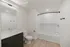 Elegant bathroom with modern black vanity, spacious bathtub, and bright lighting, featuring stylish wood flooring.