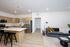 Modern open-concept kitchen and living room with sleek light wood cabinets, stainless steel appliances, and stylish seating area with a velvet sofa and contemporary decor.