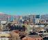 Breathtaking cityscape view with modern buildings against a backdrop of stunning snow-capped mountains and clear blue skies.