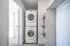 Modern in-unit laundry area with stacked washer and dryer adjacent to a hallway, featuring built-in shelving with woven baskets for storage.
