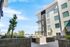 Modern apartment building with large windows and landscaped courtyard under a bright blue sky.