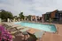 Inviting outdoor pool surrounded by comfortable lounge chairs and vibrant flowers, set against modern apartment buildings under a clear sky.