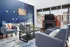 Chic communal living space with modern blue walls, comfortable seating, and fireplace, highlighted by vibrant artwork and floor-to-ceiling windows.