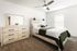 Bright and airy bedroom featuring modern wooden furniture, a stylish ceiling fan, and cozy decor accents.