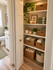 Linen storage with neatly organized wicker baskets, lush greenery, and soft lighting for a cozy feel.