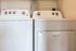 The James Apartments | Laundry room with a matching white Whirlpool washer and dryer set under a wire shelf | Luxury Apartments in Haverhill MA
