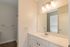 The James Apartments | Bathroom with a large mirror, single sink vanity, and bright lighting, connected to a bedroom with carpet flooring and natural light | Luxury Apartments in Haverhill MA