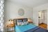 The James Apartments | Bedroom with a blue and gray color scheme, featuring a stylish bed with decorative pillows, a round metal wall art piece, and side tables with gold lamps. | Luxury Apartments Haverhill MA