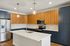 The James Apartments | Modern kitchen featuring a large island with a sink, stainless steel appliances, and a combination of wooden and blue cabinetry with pendant lighting above. | Luxury Apartments Haverhill MA