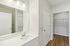 The James Apartments | View of a modern bathroom with a white vanity and large mirror, with a door leading to a walk-in closet in the background. | Luxury Apartments Haverhill MA
