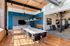 Riverwalk Lofts | Modern conference room with a long white table surrounded by black chairs. Large windows allow natural light, highlighting pendant lights above. A flat-screen TV is mounted on the blue accent wall, and the space has wooden flooring and exposed ductwork. | luxury apartments near boston