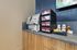 Chic coffee station with modern coffee machine, various flavor options, and an assortment of condiments in a stylish apartment lounge.