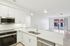 Modern kitchen with sleek white cabinetry, state-of-the-art appliances, and an inviting open-concept living space leading to large windows.