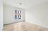 Bright and spacious bedroom with sleek wooden flooring and a large window offering a vibrant urban view.