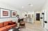 Modern apartment interior showcasing a chic open-plan kitchen and living area with stylish orange sofa, elegant artwork, and contemporary furnishings.