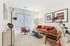 Chic living room with a modern orange sofa, stylish wooden chairs, and contemporary decor, bathed in natural light from large windows with vertical blinds.