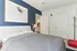 Cozy modern bedroom with elegant blue accent wall, stylish artwork, and plush bedding, offering a serene and inviting ambiance.