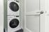 Modern apartment laundry area featuring sleek, high-efficiency stacked washer and dryer behind a stylish louvered door.
