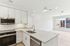 Modern kitchen with sleek white cabinetry, stainless steel appliances, and an open layout leading to a bright living area with large windows.