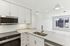 Bright and modern kitchen featuring sleek white cabinetry, quartz countertops, stainless steel appliances, and a large window offering cityscape views.
