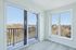 Bright and airy apartment view with sleek sliding glass doors opening to a balcony, offering stunning panoramic vistas of the city skyline and lush greenery.
