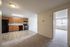 Bright apartment with modern kitchen featuring warm wood cabinets, black appliances, and tile flooring leads to a spacious living area with large windows and ample natural light.