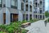 Modern apartment facade with sleek design, large windows, landscaped greenery, and inviting walkway seating.