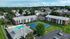 Aerial view of Princeton Place Apartments in Worcester, MA, featuring brick buildings, parked cars, a swimming pool, and tennis court, all nestled among trees and residential houses under a partly cloudy sky.