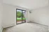 Bright apartment room with plush carpet, sliding glass doors leading to a lush green outdoor space, and modern air conditioning unit.