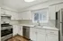 Princeton Belvidere Apartments | Modern kitchen in an apartment in Lowell, MA featuring white cabinets, stainless steel appliances, a gas stove, dishwasher, double sink under a window with vertical blinds, wood flooring, ample countertop space, and bright overhead lighting. | Apartments with Air Conditioning in Lowell