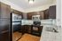 Princeton Westford Apartments | 	Modern kitchen in an apartment in Westford, MA, featuring dark wood cabinets, stainless steel refrigerator, black stove and microwave, granite countertops, under-cabinet lighting, white tile backsplash, and wood flooring. | apartments with a dishwasher in westford