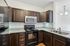 Princeton Westford Apartments | Modern kitchen in an apartment in Westford, MA, features dark wood cabinets, granite countertops, stainless steel microwave, black electric stove and fridge. Double sink and hanging light fixtures complement the light tile backsplash and wood flooring. | Apartments with Air Conditioning in Westford