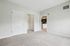 Princeton Westford Apartments | Empty room with light-colored carpet, white walls, and two closed white doors. An open doorway leads to a hallway and a glimpse of a kitchen with brown cabinets and stainless steel appliances—ideal apartment in Westford, MA. | Apartments with EV Charging in Westford