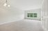 Princeton Westford Apartments | Spacious, empty room in an apartment in Westford MA, featuring light carpet, white walls, a ceiling light fixture, and large windows that fill the space with natural light and views of green trees outside. | One bedroom apartments in westford