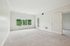 Princeton Westford Apartments | Empty, carpeted room with white walls, large window, and glass door leading outside in an apartment in Westford, MA. An open door reveals an adjoining room. The space is well-lit with natural light and features simple white trim and baseboards.| Two bedroom apartments in westford