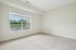 Princeton Westford Apartments | A bright, empty room in an apartment in Westford MA features beige carpet, light-colored walls, a large window with white blinds, and a view of trees and rooftops. Electrical outlets are visible on the wall. | Pet Friendly Apartments in Westford