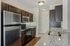 Princeton Westford Apartments | Modern kitchen in an apartment in Westford, MA, featuring stainless steel appliances, dark wood cabinets, granite countertops, a double sink, electric stove, built-in microwave, light-colored walls, wood floors, and recessed lighting. | Apartments with EV Charging in Westford