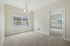 Princeton Westford Apartments | A bright, empty room in an apartment in Westford, MA features beige carpet, light-colored walls, a ceiling light fixture, and a large window. An open doorway leads to another similar carpeted room with windows. | Apartments with Balcony in Westford