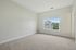 Princeton Westford Apartments | Bright, empty beige-carpeted room with white walls in an apartment in Westford, MA. Large window offers a view of a neighboring building and greenery; doorway on the right. Abundant natural light fills the space. | Apartments with Air Conditioning in Westford